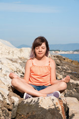 Teen girl is sitting in lotus position on the stone at coast of sea
