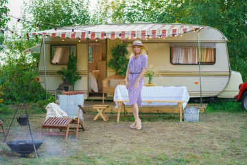 a cute woman with wavy blonde hair in a trendy summer striped dress on the background of a trailer camper van rests
