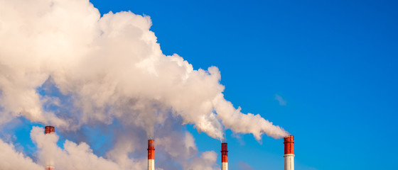 Pipes of a thermal station with clubs of white steam against a blue sky - global warming concept,...