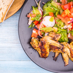 Tasty fried chicken wings with vegetable salad on a dark plate close-up and a piece of bread
