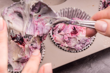 Cooking cupcakes - woman's hands lay dough with berries in a baking dish close-up