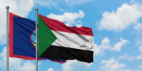 Guam and Sudan flag waving in the wind against white cloudy blue sky together. Diplomacy concept, international relations.