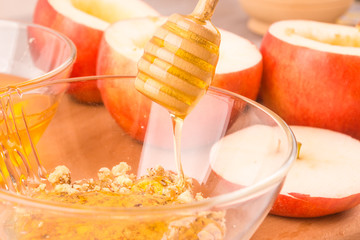 Honey pours with sticks in a bowl of honey with grated nuts, apples in the background - cooking baked apple with nuts and honey