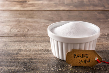 Baking soda in white bowl on wooden table. Copy space	