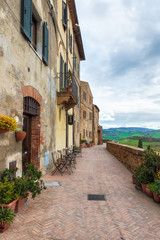 Fototapeta na wymiar A narrow picturesque medieval street along the city wall and view to the valley in old town of Pienza in Tuscany, Italy