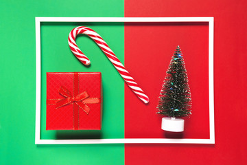 Christmas composition with present box, decorative fir tree, lollipop  on red and green background with white frame. Winter holiday concept.