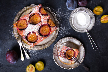 Tasty plum cake with pieces of fruit and powdered sugar on a dark background