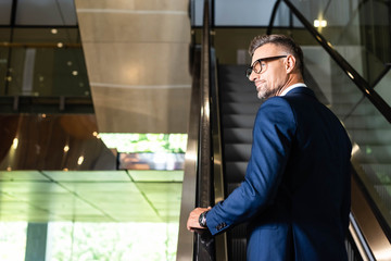 back view of handsome businessman in suit and glasses on escalator