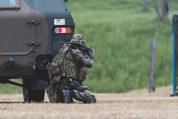 装甲車の陰で銃を構える自衛官