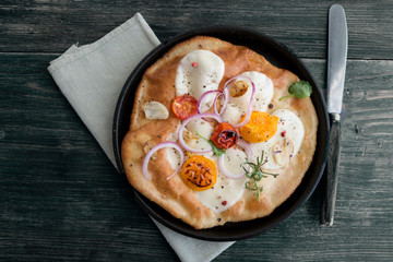 Small homemade pizza with mozzarella cheese, tomatoes, herbs on rustic wooden table. Top view. Copy space.