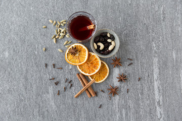 christmas and seasonal drinks concept - hot mulled wine, dry orange slices, raisins with cashew nuts and aromatic spices on grey background