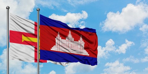 Guernsey and Cambodia flag waving in the wind against white cloudy blue sky together. Diplomacy...