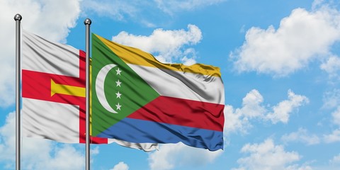 Guernsey and Comoros flag waving in the wind against white cloudy blue sky together. Diplomacy concept, international relations.