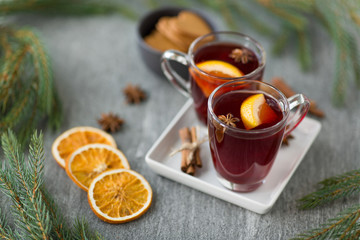 christmas and seasonal drinks concept - hot mulled wine, dry orange slices, gingerbread and aromatic spices on grey background
