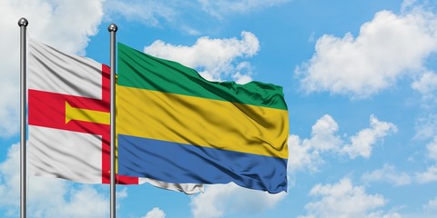 Guernsey and Gabon flag waving in the wind against white cloudy blue sky together. Diplomacy concept, international relations.
