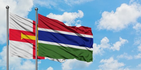 Guernsey and Gambia flag waving in the wind against white cloudy blue sky together. Diplomacy concept, international relations.