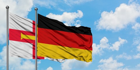 Guernsey and Germany flag waving in the wind against white cloudy blue sky together. Diplomacy concept, international relations.