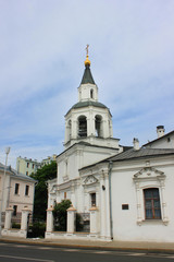 Fototapeta na wymiar Church with bell tower located on small old town street. White monastery building outdoors on narrow city street 
