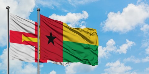 Guernsey and Guinea flag waving in the wind against white cloudy blue sky together. Diplomacy concept, international relations.