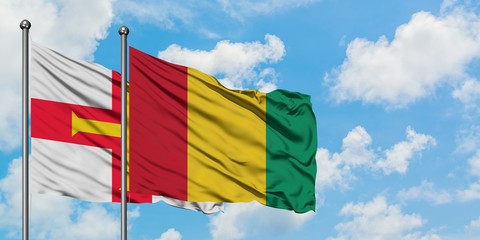 Guernsey and Guinea flag waving in the wind against white cloudy blue sky together. Diplomacy concept, international relations.