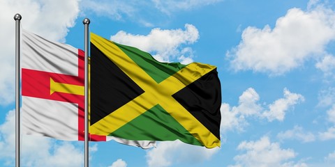 Guernsey and Jamaica flag waving in the wind against white cloudy blue sky together. Diplomacy concept, international relations.
