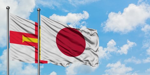 Guernsey and Japan flag waving in the wind against white cloudy blue sky together. Diplomacy concept, international relations.