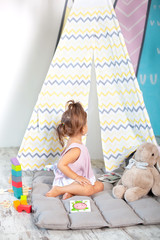 Little girl in colorful wigwam with toys. child plays with colorful toy blocks. Developing and creative toys and games for young children. child in a bedroom with rainbow bricks. child is at home.
