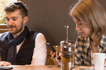 The guy and the blonde girl in a plaid shirt at a table in a cafe and a glass teapot.