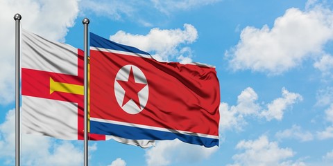 Guernsey and North Korea flag waving in the wind against white cloudy blue sky together. Diplomacy concept, international relations.