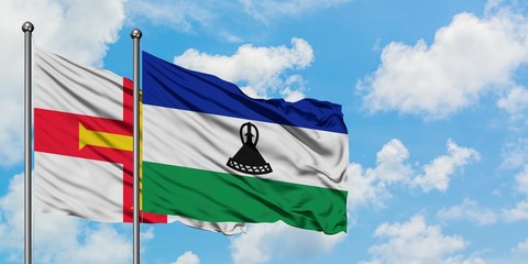 Naklejka na ściany i meble Guernsey and Lesotho flag waving in the wind against white cloudy blue sky together. Diplomacy concept, international relations.