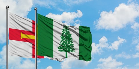Guernsey and Norfolk Island flag waving in the wind against white cloudy blue sky together. Diplomacy concept, international relations.
