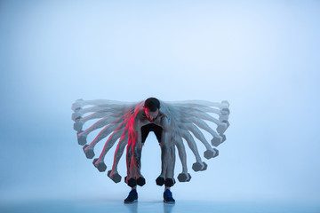 Wings. Young caucasian bodybuilder training over studio background in neon and strobe light....