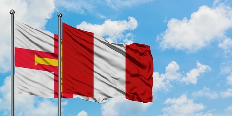 Guernsey and Peru flag waving in the wind against white cloudy blue sky together. Diplomacy concept, international relations.