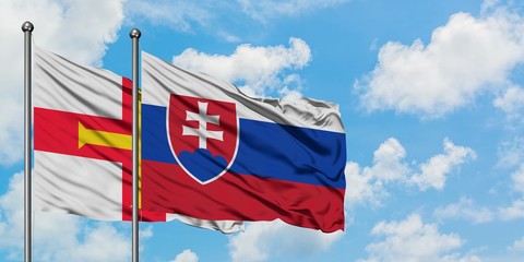 Guernsey and Slovakia flag waving in the wind against white cloudy blue sky together. Diplomacy concept, international relations.