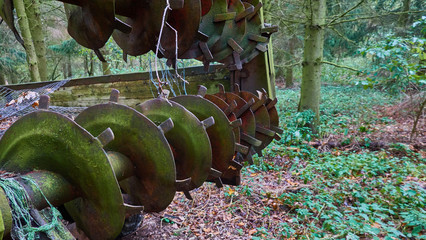 Detailed view of an old rusty harrow standing unused on a storage place in the forest.