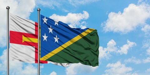 Guernsey and Solomon Islands flag waving in the wind against white cloudy blue sky together. Diplomacy concept, international relations.