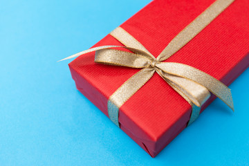 Fototapeta premium holiday, greeting and surprise concept - christmas red gift box with golden bow on blue background