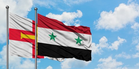 Guernsey and Syria flag waving in the wind against white cloudy blue sky together. Diplomacy concept, international relations.