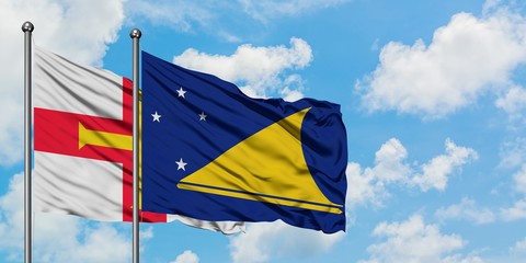 Guernsey and Tokelau flag waving in the wind against white cloudy blue sky together. Diplomacy concept, international relations.