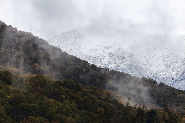 Fog in the mountains against the background of peaks with snow in the fall in Sochi, Russia.