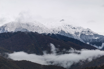Fototapeta na wymiar Fog in the mountains against the background of peaks with snow in the fall in Sochi, Russia.