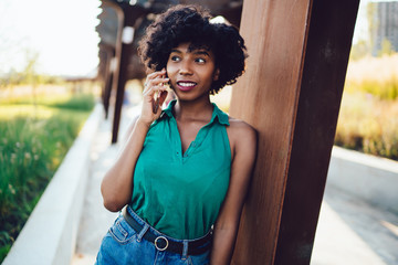 Beautiful African American hipster girl calling via modern cellular gadget,concept of technology and communication. Young dark skinned female having conversation via smartphone while standing outdoors