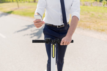 business and people and concept - close up of young businessman with smartphone and electric scooter outdoors