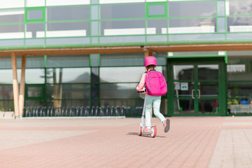 Naklejka premium education, childhood and people concept - school girl with backpack riding scooter