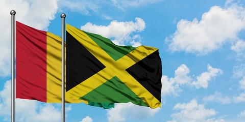 Guinea and Jamaica flag waving in the wind against white cloudy blue sky together. Diplomacy concept, international relations.