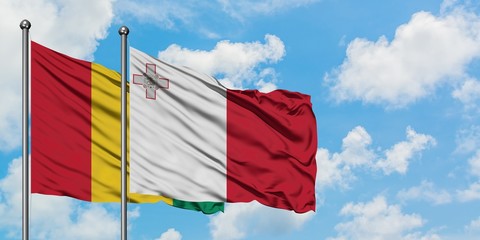 Guinea and Malta flag waving in the wind against white cloudy blue sky together. Diplomacy concept, international relations.