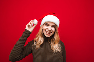 Closeup portrait of joyful girl in warm sweater and christmas hat isolated on red background, looking at camera and smiling. Happy lady in santa claus hat posing on red background.