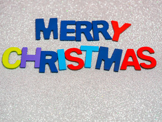 Fototapeta na wymiar Multicolored wooden alphabet of Merry Christmas text on rough gradient glitter white paper texture and background. Greeting card for Christmas holidays.