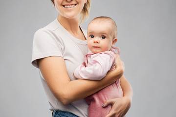 family, child and parenthood concept - happy smiling young mother holding little baby daughter over grey background