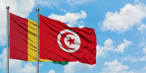 Guinea and Tunisia flag waving in the wind against white cloudy blue sky together. Diplomacy concept, international relations.